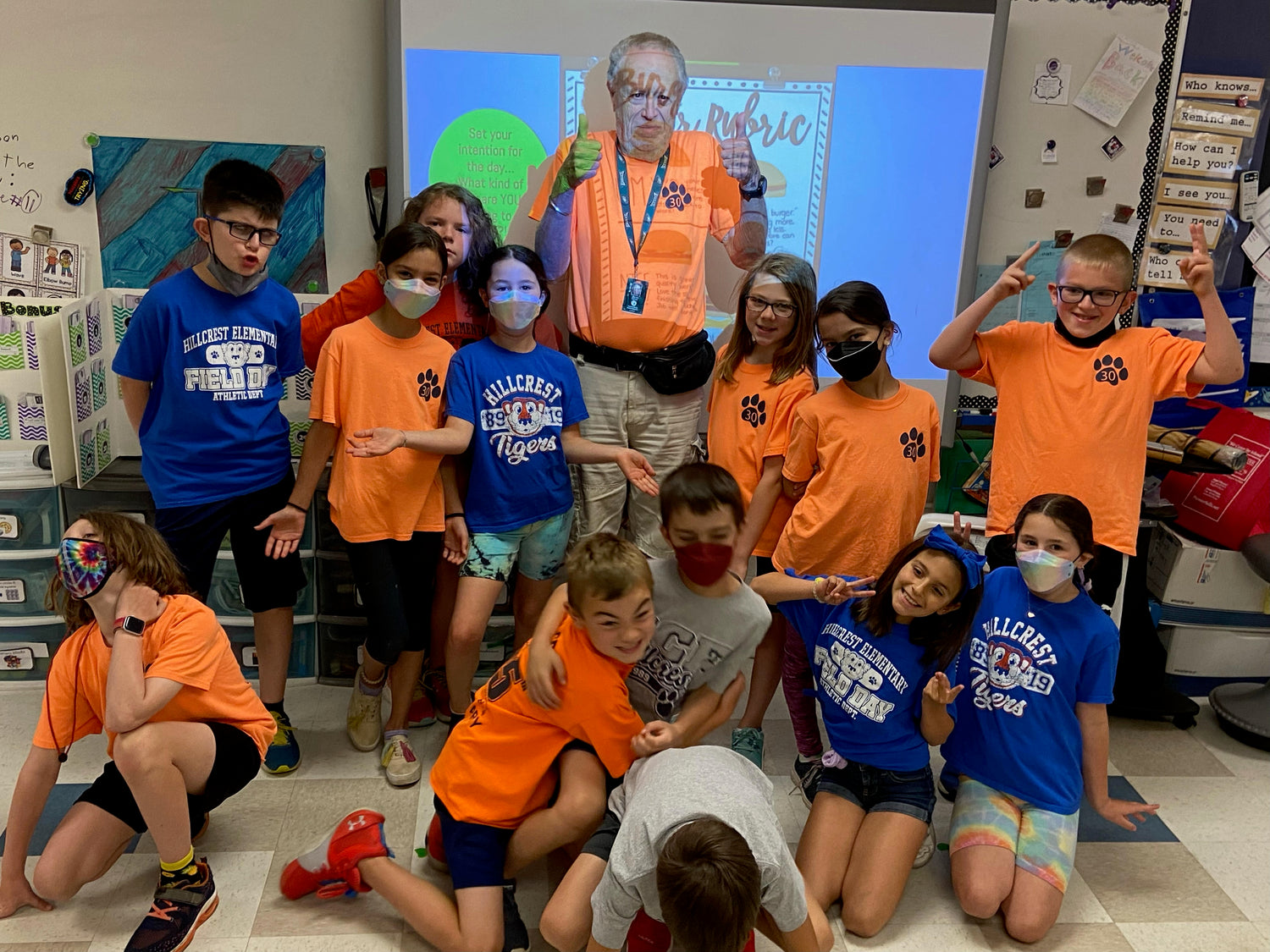 Students posing with a S.A.G.E. volunteer at the front of a classroom